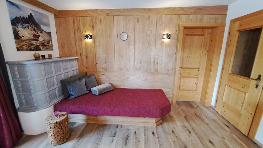 Wohnbereich im Appartement Schönangeralm mit Liege, Kachelofen und Holzverkleidung