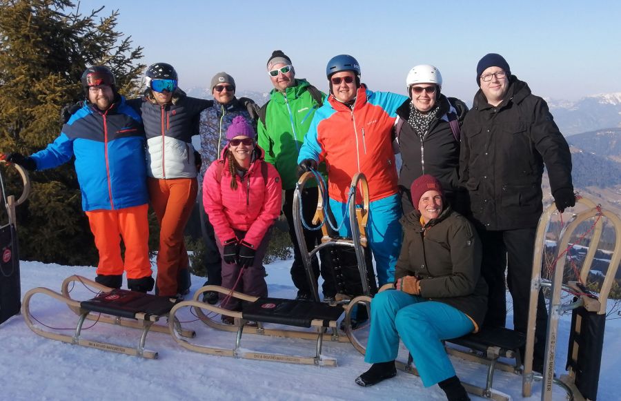 Rodelgruppe im Schnee mit Schlitten und Blick auf die winterliche Berglandschaft