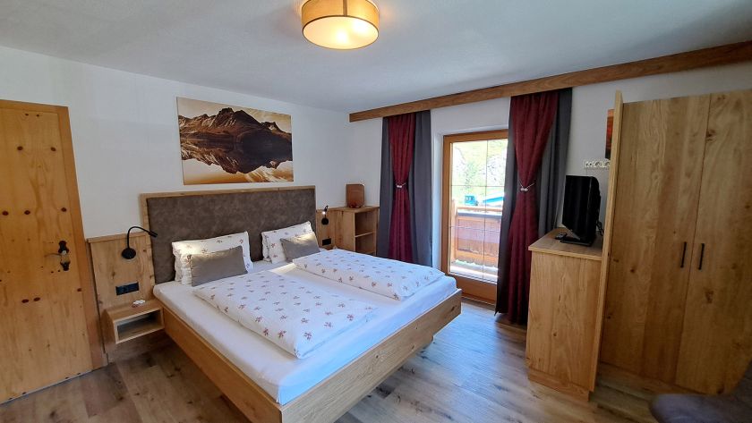 Schlafzimmer im Appartement Schönangeralm mit Doppelbett, TV und Balkonzugang