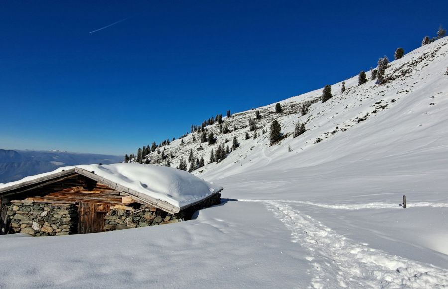 Verschneite Almhütte mit Fußspuren im Schnee und blauem Himmel in Tirol