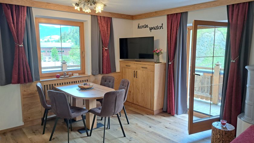 Wohn- und Essbereich im Appartement Schönangeralm mit Holztisch, TV und Balkonzugang