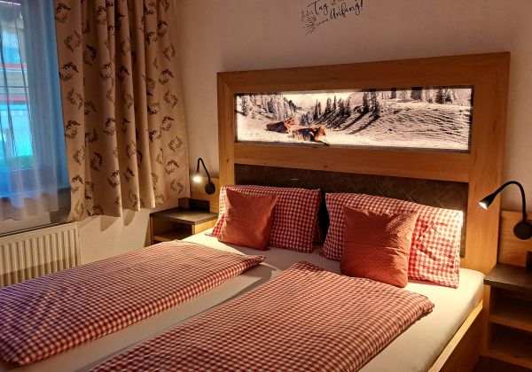 Schlafzimmer im Appartement Gratlspitz mit rot kariertem Bett und beleuchtetem Wandbild